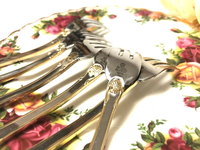 May include: Set of five silver forks with gold accents. The forks have a decorative design and are engraved with "Royal Albert 1810 1842".
