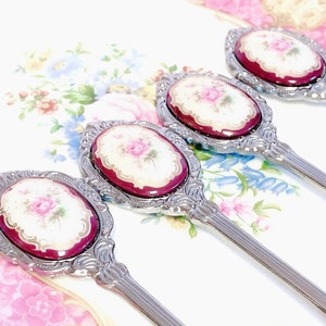 Pu&ograve; includere: Quattro cucchiaini d'argento con manici decorati e disegni floreali sulla parte superiore. I disegni floreali sono in tonalit&agrave; di rosa, bianco e oro.