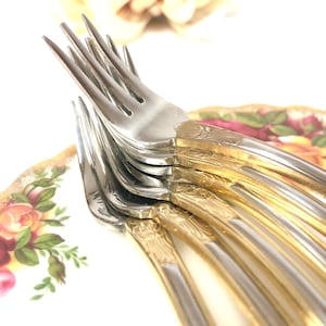May include: A stack of silver forks with gold accents on a floral patterned plate.