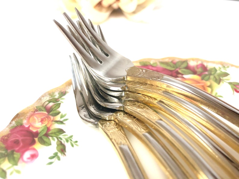 May include: A stack of silver forks with gold accents on a floral patterned plate.