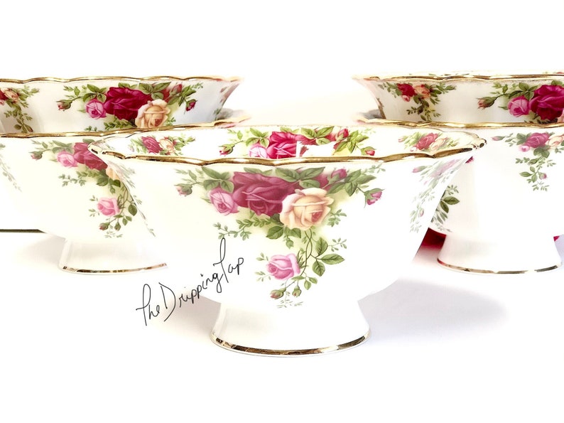 May include: Set of four white porcelain bowls with a floral pattern featuring pink, red, and yellow roses. The bowls have a scalloped edge and a gold trim.