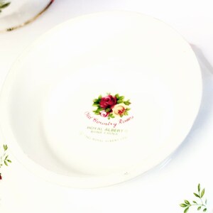 May include: Close-up of the bottom of a white teacup with a floral design. The text "Old Country Roses" is printed in pink and black, along with "Royal Albert Bone China" and "Made in England".