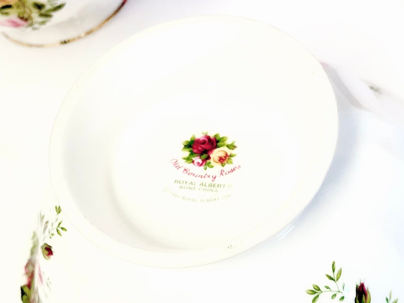 May include: Close-up of the bottom of a white teacup with a floral design. The text "Old Country Roses" is printed in pink and black, along with "Royal Albert Bone China" and "Made in England".