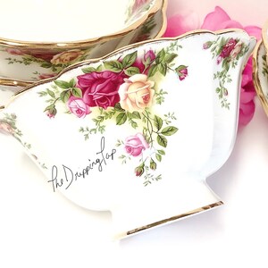 May include: A set of three white ceramic bowls with a gold rim and a floral pattern featuring red, pink, and yellow roses. The bowls are decorated with a green vine pattern and the text "the Dripping Tap".