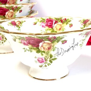 May include: A set of four white porcelain bowls with a floral pattern featuring red, pink, and yellow roses. The bowls have a gold rim and a gold trim around the base. The bowls are on a white surface. The text "the Dripping Tap" is written on the side of one of the bowls.