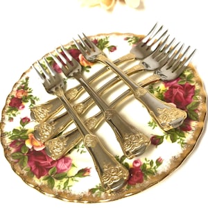 May include: Set of six gold-plated forks with ornate floral designs on a white plate with a floral pattern.