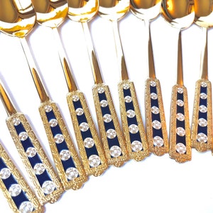 May include: A set of gold-plated teaspoons with blue and white enamel detailing. The spoons have a decorative design with a repeating pattern of circles and squares.