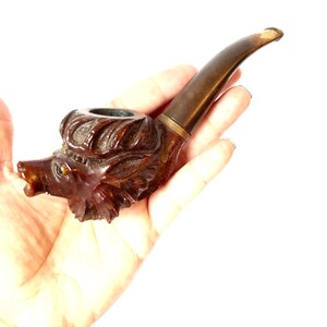 Puede incluir: Una pipa de fumar de madera tallada en forma de cabeza de lobo. La pipa es marr&oacute;n con una boquilla marr&oacute;n oscuro.