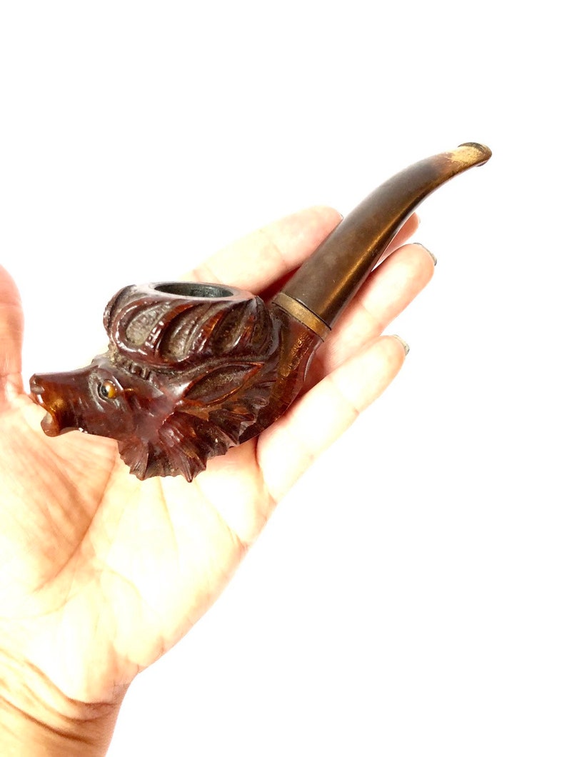 Puede incluir: Una pipa de fumar de madera tallada en forma de cabeza de lobo. La pipa es marr&oacute;n con una boquilla marr&oacute;n oscuro.