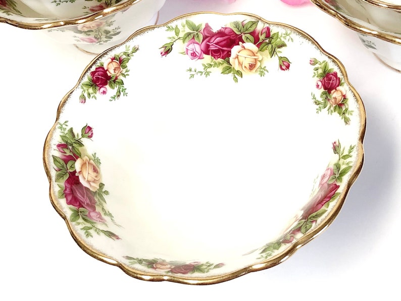 May include: A white ceramic bowl with a gold rim and a floral design featuring red, yellow, and green roses. The bowl has a scalloped edge.