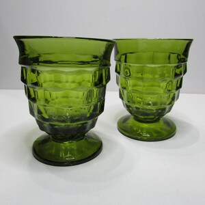 May include: Two green glass tumblers with a square patterned design. The glasses have a wide base and a flared top.
