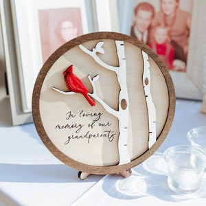 May include: A wooden round plaque with a white birch tree design and a red cardinal perched on a branch. The plaque has the text "In loving memory of our grandparents" written on it.