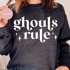 May include: A dark gray sweatshirt with the text "ghouls rule" in white with two white stars on either side of the text.