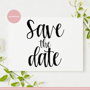 Puede incluir: Una tarjeta blanca con caligrafía negra que dice "Save the date". La tarjeta está rodeada de hojas verdes y flores blancas.