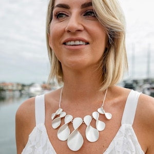 May include: A silver necklace with a unique design featuring multiple interconnected loops. The necklace is made of a smooth, polished metal and has a modern, abstract look.