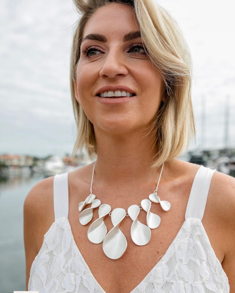 May include: A silver necklace with a unique design featuring multiple interconnected loops. The necklace is made of a smooth, polished metal and has a modern, abstract look.