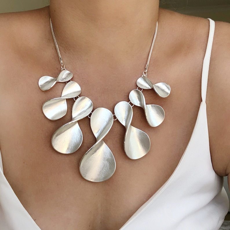 May include: A silver necklace with a modern design featuring multiple interconnected, twisted, and elongated teardrop-shaped pendants.