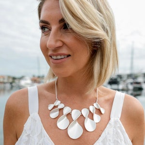 May include: A silver statement necklace with a unique, organic design. The necklace features multiple interconnected, teardrop-shaped pieces that create a flowing, asymmetrical look.