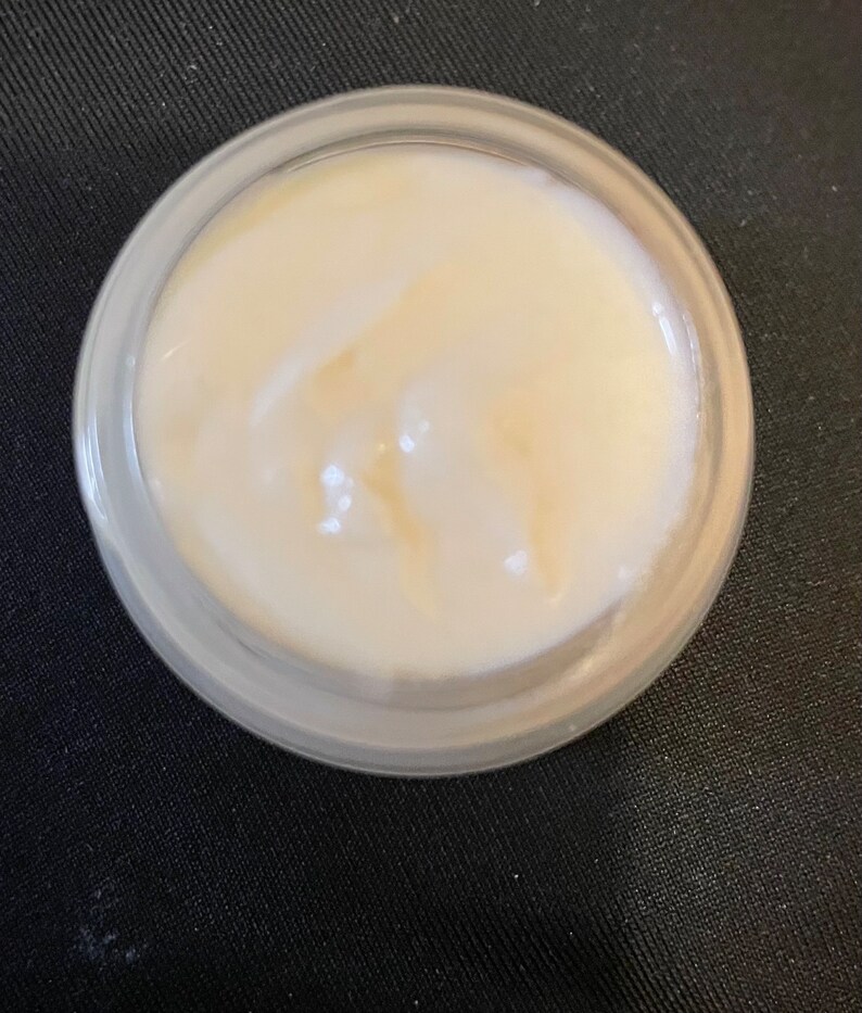 May include: A small glass jar filled with a white cream. The cream has a smooth, creamy texture.
