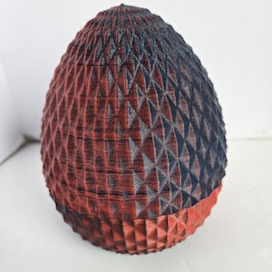 Pode incluir: Objeto decorativo em forma de ovo com um padrão geométrico texturizado. A metade superior é azul escuro, passando para vermelho na parte inferior. A superfície tem um padrão de diamante repetido, criando uma textura visual única.