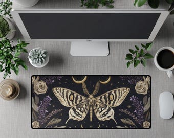 Op de afbeelding: Een zwarte rechthoekige bureaumat met een grote motillustratie met crème- en bruintinten. De mat bevat ook crèmerozen, lavendel en halve manen. Een computer, planten en een kopje koffie omringen de bureaumat.
