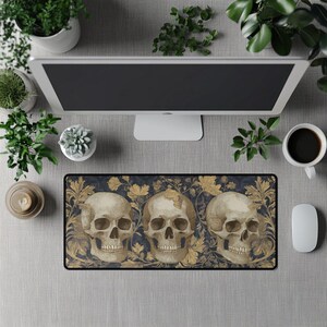 Puede incluir: Alfombrilla de ratón rectangular con tres calaveras detalladas y un estampado floral en dorado y crema sobre un fondo azul oscuro. La alfombrilla está rodeada por un borde negro.