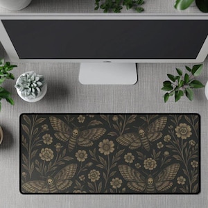 May include: A black desk mat featuring a repeating pattern of moths and floral elements in brown and gold tones. The mat is rectangular and positioned under a computer monitor, with a white mouse and coffee cup. The design has a gothic and nature-inspired aesthetic.