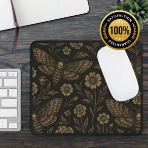 May include: Rectangular black mousepad featuring a gold moth and floral pattern. The moth design includes a skull motif. A white computer mouse rests on the pad. A keyboard and notebook are also visible.
