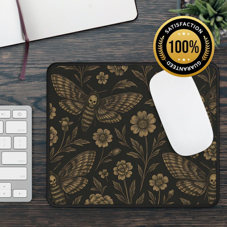 May include: Rectangular black mousepad featuring a gold moth and floral pattern. The moth design includes a skull motif. A white computer mouse rests on the pad. A keyboard and notebook are also visible.