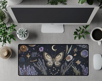 Op de afbeelding: Een zwarte rechthoekige bureaumat met een vlinderontwerp, een halve maan en sterren. De mat heeft een donkere achtergrond met bloemen en botanische elementen, waaronder lavendel en rozen. Een computermonitor, een koffiekopje en een muis zijn ook zichtbaar.