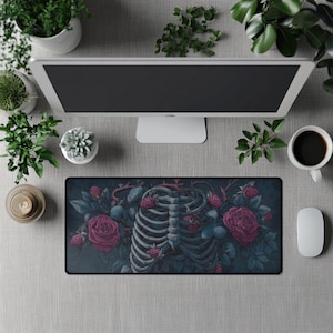 Puede incluir: Una alfombrilla de ratón rectangular con un fondo azul oscuro y una ilustración detallada. El diseño incluye una caja torácica humana, rosas rojas y frambuesas. La alfombrilla está rodeada por un borde negro.