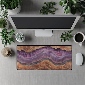 May include: A rectangular mouse pad with a black border features a layered design in shades of brown, purple, and gray, resembling a cross-section of stone or wood. The desk setup includes a computer monitor, coffee cup, mouse, and potted plants.