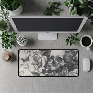 Puede incluir: Alfombrilla de ratón rectangular con un diseño floral y de calavera en blanco y negro. El diseño incluye rosas, una mariposa y una calavera humana. La alfombrilla tiene un borde negro y está sobre una superficie gris.