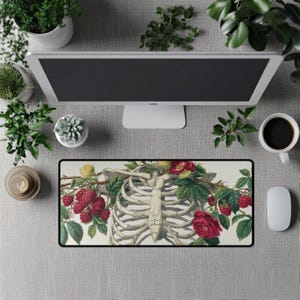 Puede incluir: Alfombrilla de ratón rectangular con una ilustración detallada de una caja torácica humana adornada con rosas rojas, flores amarillas y frambuesas. El diseño está sobre un fondo blanco con un borde negro. La alfombrilla está sobre una superficie gris.