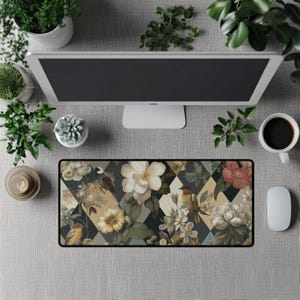 Può includere: Un tappetino per mouse rettangolare con un design floreale e di uccelli. Il tappetino presenta un motivo a rombi con colori crema, nero e verde oliva. Il design include fiori bianchi e gialli e uccelli. Sono visibili anche un monitor del computer, una tazza di caffè e un mouse.