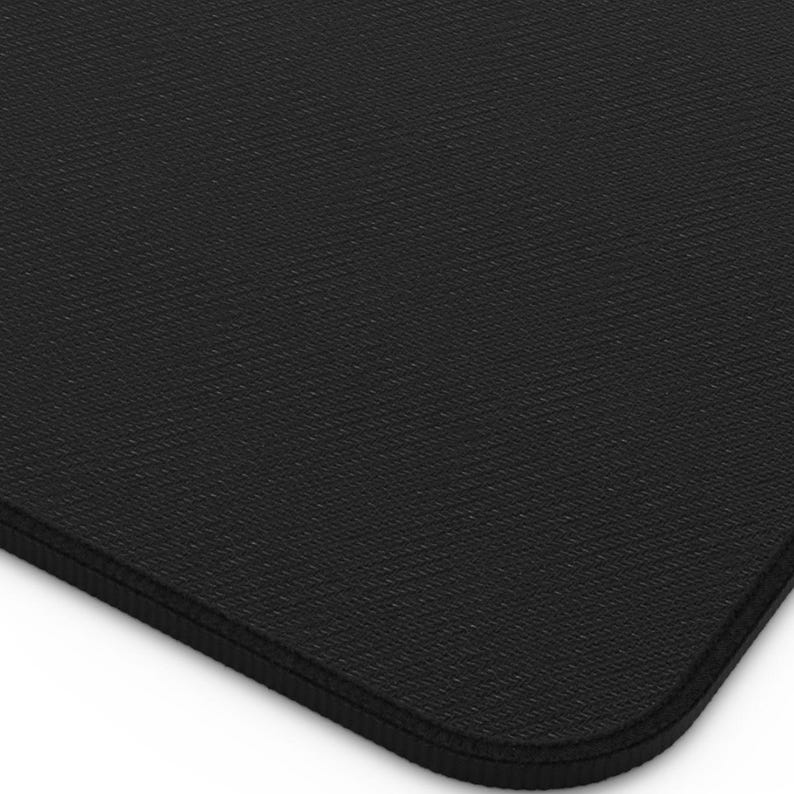 May include: A close-up of a black rectangular mat with a textured surface. The mat has rounded corners and a stitched edge. The mat is likely used for a desk or workspace.