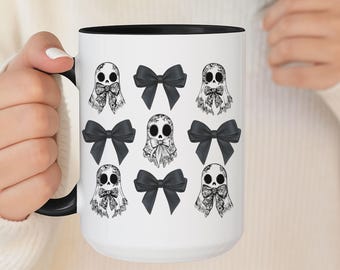 May include: White ceramic mug with a black interior and handle. The mug features a repeating pattern of ghost illustrations with bows and black bows. The design is in black and white.