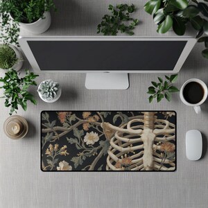 Puede incluir: Una alfombrilla de ratón rectangular con una ilustración detallada de una caja torácica humana y elementos florales sobre un fondo oscuro. El diseño incorpora tonos beige, marrón y blanco, creando una estética única y artística. La alfombrilla está rodeada por un borde negro.