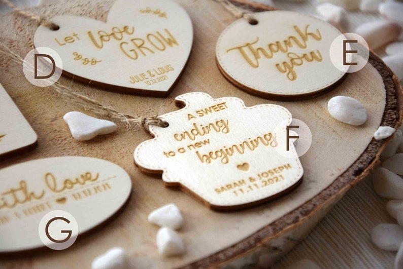K&ouml;nnte beinhalten: Ein Set aus sechs Holz-Hochzeitsgeschenkanh&auml;ngern mit goldener Beschriftung. Die Anh&auml;nger zeigen verschiedene Spr&uuml;che, darunter "Lass die Liebe wachsen", "Ein s&uuml;&szlig;es Ende f&uuml;r einen neuen Anfang" und "Danke".