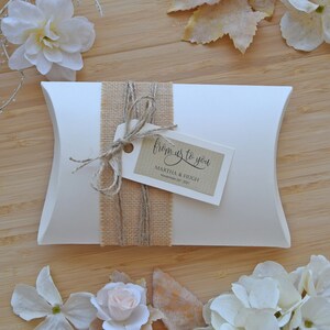 May include: White pillow box with a burlap ribbon and a brown tag that says "from us to you" with the names Martha & Hugh and the date November 24, 2019.
