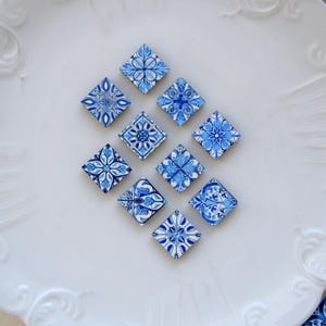 Könnte beinhalten: Zehn blaue und weiße Keramikfliesen mit komplizierten floralen Mustern, die in einer Diamantform auf einem weißen Teller angeordnet sind.