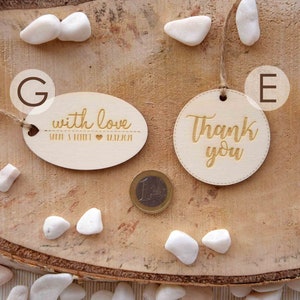 K&ouml;nnte beinhalten: Zwei Holz-Geschenk-Etiketten mit goldener Beschriftung. Eine Etikette ist oval geformt und sagt "with love" mit einem Herzen und Namen. Die andere Etikette ist rund und sagt "Thank you".