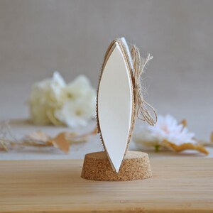 May include: A white oval-shaped sign with a cork base and twine tied around it. The sign is blank and ready for personalization.
