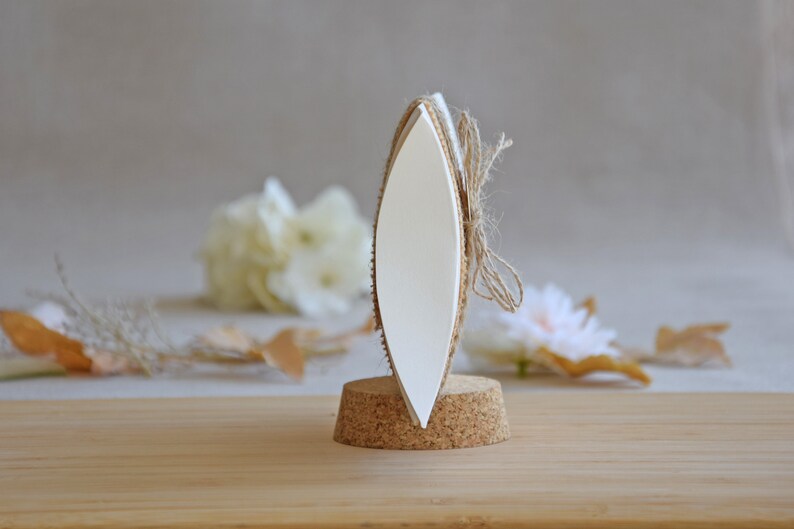 May include: A white oval-shaped sign with a cork base and twine tied around it. The sign is blank and ready for personalization.