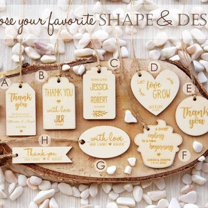 K&ouml;nnte beinhalten: Sortiment aus Holz-Hochzeitsgeschenkanh&auml;ngern in verschiedenen Formen und Designs. Die Anh&auml;nger zeigen den Text "Danke", "Mit Liebe", "Lass die Liebe wachsen", "Ein s&uuml;&szlig;er Abschluss f&uuml;r einen neuen Anfang" und "Mit Liebe".