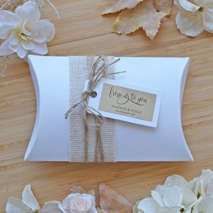 May include: A white pillow box with a brown burlap ribbon and a brown paper tag that says "from us to you" with the names Martha & Hugh and the date November 20, 2021.