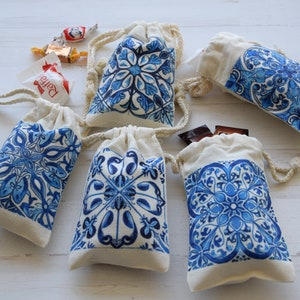 May include: Five small white fabric drawstring bags with blue and white tile patterned designs. The bags are on a white wooden surface.