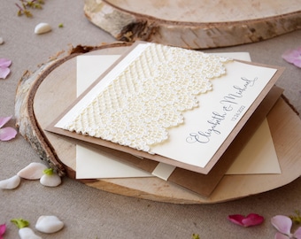 Puede incluir: Una invitación de boda con cartulina marrón y crema. La tarjeta presenta un borde de encaje blanco y el texto "Elizabeth & Michael" con la fecha "12.24.2021".