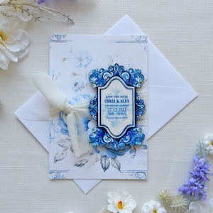 May include: Blue and white wedding save the date card with a decorative frame and the text "Save the Date Chris & Alex and getting married 07.12.20XX" printed on it.