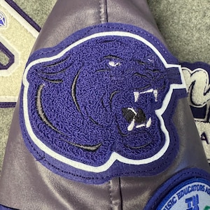 May include: Purple leather jacket with a blue and white panther patch on the sleeve. The jacket also has a blue and white patch with the text "Texas Music Educators Association" and a musical symbol.